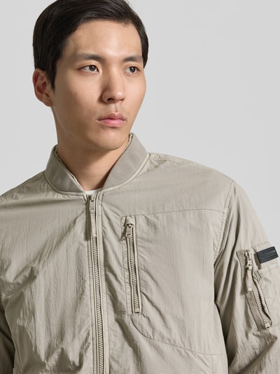 Männermodel trägt khujo Blouson mit Label-Patches Modell 'IBE' in Beige mit Reißverschluss und Brusttasche, Nahaufnahme Oberkörper.