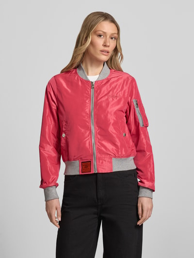 Frauenmodel trägt Bomberjacke mit Label-Patch und Reißverschlusstasche am Ärmel von Original Bombers, Lockerer-Schnitt, Stehkragen, Ganzkörperansicht von vorne.