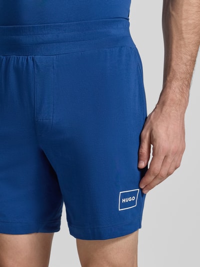 Männermodel trägt Regular Fit Sweatshorts aus Baumwoll-Mix Modell 'LAZE SHORTS CW' von HUGO, Optik: Unifarben, Label-Print, Bundabschluss: Elastisch, Nahaufnahme Oberkörper.