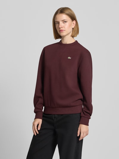 Modelka nosi Relaxed Fit Sweatshirt aus Baumwoll-Mix od Lacoste w kolorze bordowym, gładka tekstura, damska bluza, zdjęcie całej sylwetki z przodu.