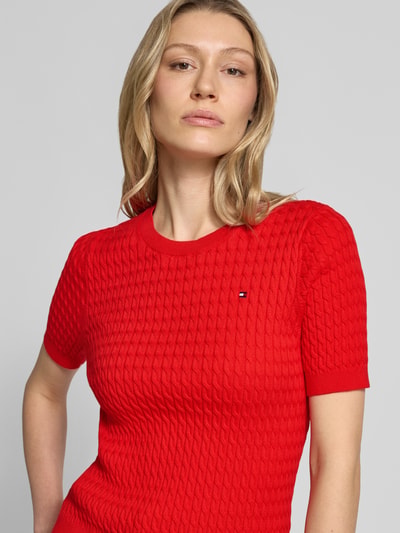 Frauenmodel trägt Slim Fit T-Shirt aus reiner Baumwolle von Tommy Hilfiger, Optik: Unifarben, Zopfmuster, Logo-Detail, Rundhals, Kurzarm, Strick, Ganzkörperansicht von vorne.