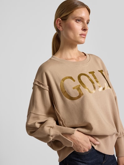Frauenmodel trägt Oversized Sweatshirt aus reiner Baumwolle mit Statement-Print von miss goodlife in Beige mit Goldprint, Rundhalsausschnitt, elastische Abschlüsse, Nahaufnahme Oberkörper.