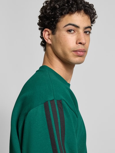 Männermodel trägt Sweatshirt mit Logo und Rundhalsausschnitt von adidas Sportswear, Baumwoll-Viskose-Mix, Relaxed-Fit, Nahaufnahme Oberkörper.