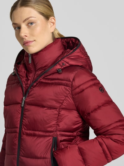 Frauenmodel trägt Steppjacke mit Kapuze und Reißverschlusstaschen von MICHAEL Michael Kors in Dunkelrot, Nahaufnahme Oberkörper.