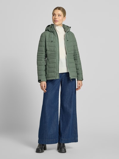 Vrouwenmodel draagt Jacke mit Kapuze und Label-Patch Modell van G.I.G.A. DX in groene kleur, recht model, met capuchon, labelpatch, ritssluiting, zijritszakken, mouwsluitingen met klittenband, waterdicht tot 10.000 mm, volledige lengte voorkant.