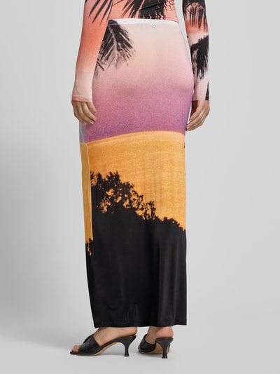 Frauenmodel trägt Maxirock aus Viskose-Mix von Rabanne mit Allover-Foto-Print in orange, lila und schwarz, elastischer Bund, Ganzkörperansicht Rückansicht.