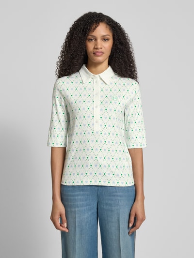 Frauenmodel trägt Slim Fit Poloshirt mit Logo-Applikation von Marc Cain, Allover-Motiv-Print, elastischer Baumwoll-Mix, Halbarm, Polokragen, weiß-grün, Ganzkörperansicht von vorne.