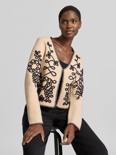 Modelka nosi Strickjacke im Allover-Look mit Hakenverschluss von Apricot, beżowy z czarnym wzorem, krój regular fit, V-dekolt, długość tyłu w rozmiarze S: 29 cm, długość rękawa w rozmiarze S: 63 cm, widok całej sylwetki z przodu