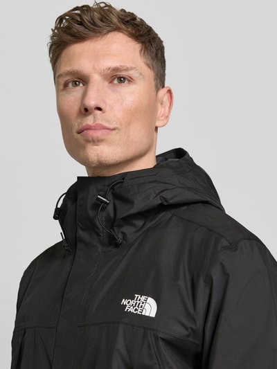 Männermodel trägt Jacke mit Kapuze von The North Face in Schwarz mit Label-Print, Reißverschlusstaschen, Nahaufnahme Oberkörper.
