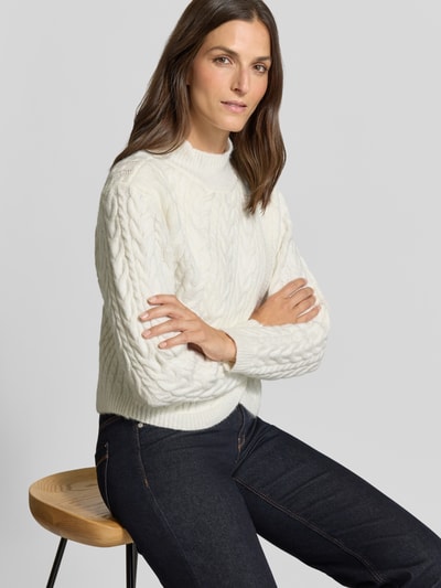 Frauenmodel trägt Strickpullover mit Woll-Anteil in Wickel-Optik von Apricot in Weiß mit Zopfmuster, Stehkragen, Material-Mix, Nahaufnahme Oberkörper.