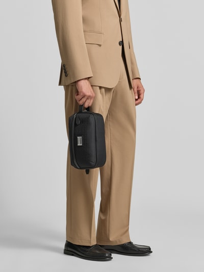 Männermodel trägt Kulturbeutel mit Label-Applikation von Emporio Armani, schwarzer Farbton, rechteckige Form, Ganzkörperansicht von vorne. Hauptfach mit Reißverschluss, Logo-Print, Innentasche mit Reißverschluss, variable Maße und Schulterriemenlänge.