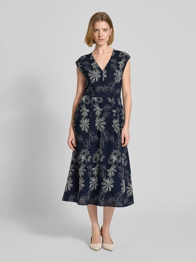 Frauenmodel trägt Midikleid mit Stitchings und Eingrifftaschen von Milano Italy, dunkelblauer Baumwoll-Mix, A-Linie, V-Ausschnitt, florale Muster, Ganzkörperansicht von vorne.