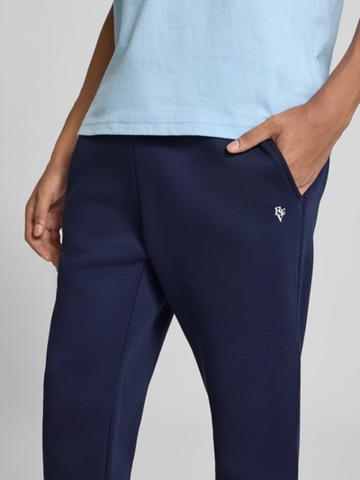 Männermodel trägt granatowe Slim Fit spodnie dresowe 'Slim Fit Sweatpants aus Baumwoll-Mix' von REVIEW z mieszanki bawełny, krój slim fit, elastyczny pas z tunelem, wpuszczane kieszenie boczne, kieszeń z tyłu, wyhaftowane logo; długość wewnętrzna nogawki w rozmiarze M: 79 cm, widok z przodu, zbliżenie na biodra.