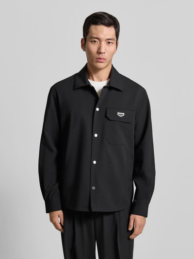 Männermodel trägt Hemdjacke mit Label-Detail von Antony Morato in Schwarz, lockerer Schnitt, sichtbare Druckknopfleiste, Ganzkörperansicht von vorne.