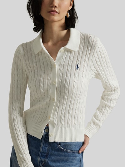 Modelka kobieca nosi Slim Fit Strickjacke aus reiner Baumwolle von Polo Ralph Lauren, biała, krój slim fit, wzór warkoczowy, logo, z dzianiny, bawełna, zapięcie na guziki, długi rękaw, prążkowane wykończenia, z kołnierzykiem, jednolita. Zbliżenie na górną część ciała z przodu.