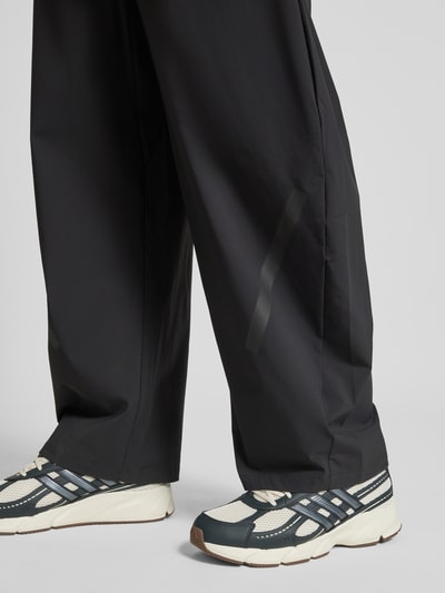 Männermodel trägt Oversized Jogpants mit Reißverschlusstaschen von adidas Sportswear im Elastischer-Material-Mix, Farbe Schwarz, Ganzkörperansicht von vorne.