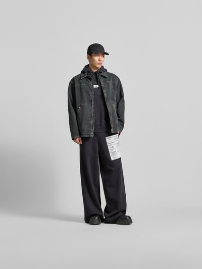 Männermodel trägt Hoodie mit Label-Stitching von MM6 Maison Margiela in Schwarz, lockere Passform, Ganzkörperansicht von vorne.