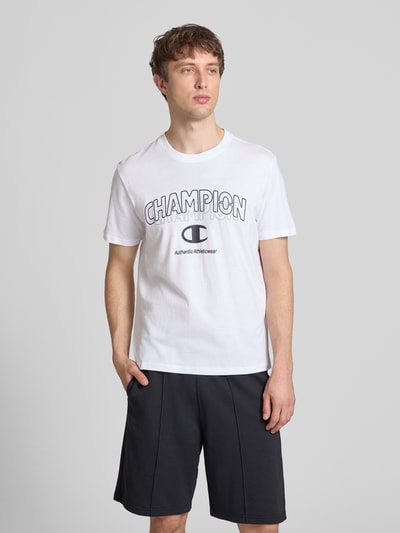 Männermodel trägt weißes T-Shirt mit Label-Print und Rundhalsausschnitt von CHAMPION, reine Baumwolle, Regular Fit, Ganzkörperansicht von vorne.