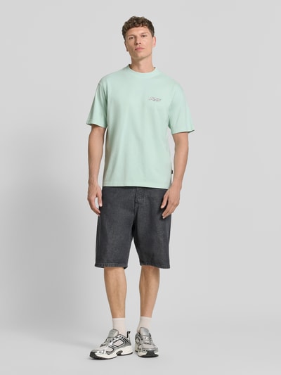Männermodel trägt Regular Fit T-Shirt aus reiner Baumwolle Modell 'SURFWASH' von BOSS Orange in Hellgrün mit Label Print, unifarben, Ganzkörperansicht von vorne.