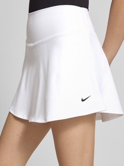 Frauenmodel trägt Minirock im 2-in-1-Look mit Logo von NIKE TRAINING in Weiß, A-Linie, elastischer Bund, Nahaufnahme Oberschenkel.