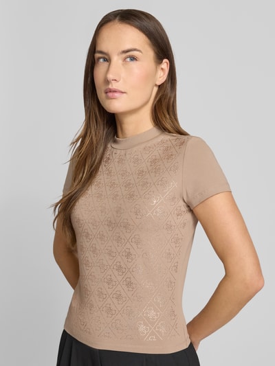 Vrouwenmodel draagt Slim Fit T-Shirt met Allover-Strasssteinbesatz van Guess in beige met logo detail en opstaande kraag, borst close-up vooraan.