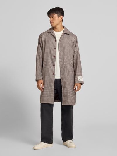 Männermodel trägt Trenchcoat mit Knopfleiste und Label-Patch von ANOTHER COTTON LAB, karierte Struktur, gedeckte Farben, Ganzkörperansicht von vorne