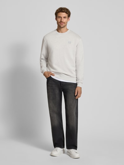 Männermodel trägt Regular Fit Sweatshirt aus reiner Baumwolle mit Label-Patch von Scotch & Soda in Hellgrau, Ganzkörperansicht von vorne. Reine Baumwolle, elastische Abschlüsse, Rückenlänge und Ärmellänge wie bei Größe M, dezente Struktur.