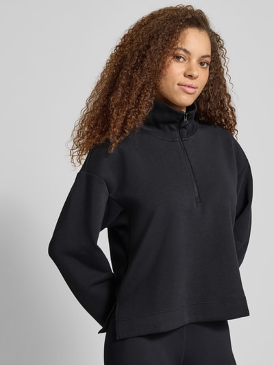 Frauenmodel trägt Relaxed Fit Sweatshirt mit Reißverschluss von adidas Sportswear in Schwarz mit Rollkragen und überschnittenen Schultern, Nahaufnahme Oberkörper.