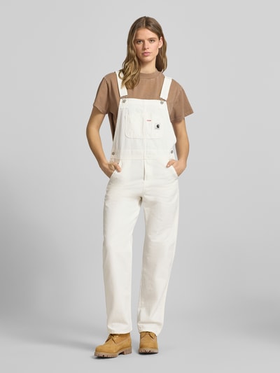 Frauenmodel trägt Overall mit Brusttasche Modell 'BIB' von Carhartt Work In Progress aus Reine Baumwolle mit Straight Fit in Creme, Ganzkörperansicht von vorne. Eingrifftaschen, Gesäßtaschen, Karree-Ausschnitt, Label-Patch, Rückenlänge bei Größe S: 48 cm, Brustweite: 38 cm, Gesamtlänge: 150 cm, Innenbeinlänge: 76 cm.