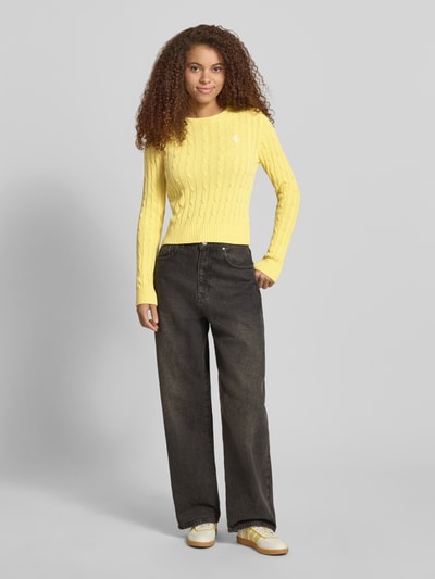 Frauenmodel trägt Strickpullover mit Zopfmuster und Label-Stitching von REVIEW in Gelb aus Baumwoll-Mix, Regular-Fit, Ganzkörperansicht von vorne.