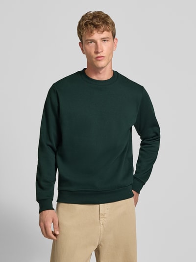 Männermodel trägt Regular Fit Sweatshirt mit Baumwoll-Anteil Modell 'Bradley' von JACK & JONES in Dunkelgrün, Ganzkörperansicht von vorne. Material-Mix, Rundhalsausschnitt, Langarm, gerippte Abschlüsse, Logo-Label dezent, Rückenlänge 66 cm, Ärmellänge 64 cm, schlichte Struktur.