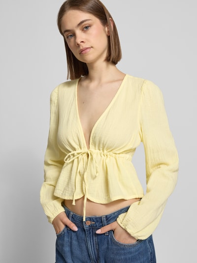 Frauenmodel trägt Regular Fit Langarmbluse aus reiner Baumwolle Modell 'SASTINA' von Pieces, Optik: Unifarben, V-Ausschnitt, Musselin-Textur, Bindeverschluss, Ganzkörperansicht von vorne.