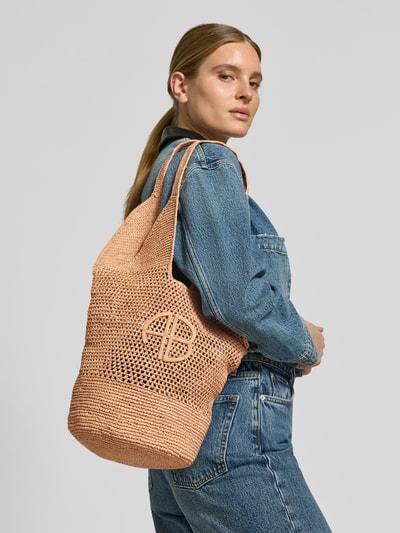 Vrouwenmodel draagt Shopper met Label-Applikation van Anine Bing in beige met semitransparante look, open hoofdvak, gatenpatroon, korte hengsels, breedte 36 cm, lengte 30 cm, diepte 19 cm, detailopname schouderpartij.