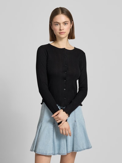 Frauenmodel trägt Slim Fit Cardigan aus Baumwoll-Viskose-Mix Modell 'MARIE' von Pieces in Schwarz, Lochstrickmuster, einreihige Knopfleiste, Rundhals, Langarm, Frill, Melange-Optik, Ganzkörperansicht von vorne.