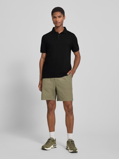 Männermodel trägt schwarzes Regular Fit Poloshirt aus reiner Baumwolle von s.Oliver RED LABEL, Ganzkörperansicht von vorne.