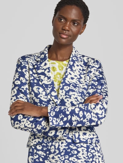 Kobiece model prezentuje żakiet Slim Fit Blazer mit Pattentaschen von Marc Cain, Mieszanka materiałów z dodatkiem streczu, wzór na całej powierzchni, Kołnierz z połami, kieszenie z patką, zapięcie na guzik, Długość tyłu w rozmiarze 36: 66 cm, Szerokość w rozmiarze 36: 47 cm, Długość rękawów w rozmiarze 36: 60 cm. Nahaufnahme Oberkörper.