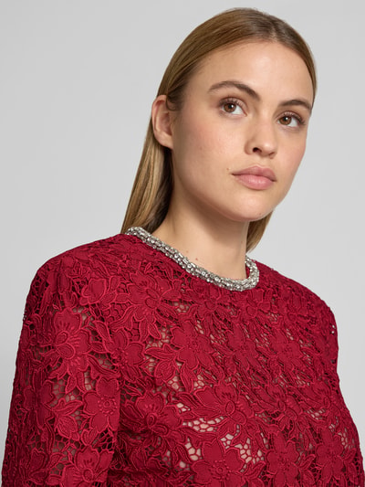 Frauenmodel trägt Slim Fit Longsleeve aus floraler Spitze von Self-Portrait in Rot mit Ziersteinbesatz, semitransparent, Nahaufnahme Oberkörper.