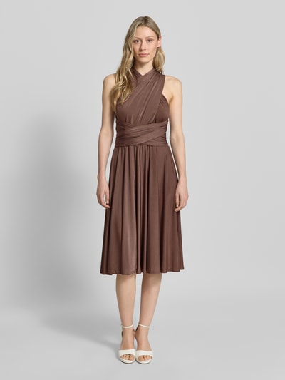 Frauenmodel trägt knielanges Cocktailkleid mit tiefem V-Ausschnitt von Rose Avenue in Braun, Taillierter Schnitt, Taillenband, Ganzkörperansicht von vorne.