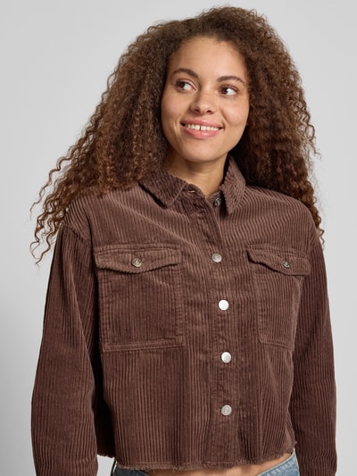Frauenmodel trägt Boxy Fit Cordjacke aus reiner Baumwolle Modell 'MARINA-ENY LIFE' von Only in Braun mit Knopfleiste und Brusttaschen, Cordstruktur, unifarben, Nahaufnahme Oberkörper.