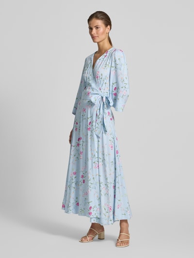 Frauenmodel trägt Wickelkleid mit V-Ausschnitt Modell 'SAVANNA' von YAS in Hellblau mit floralen Mustern aus reiner LENZING™-ECOVERO™-Faser, Taillierter Schnitt, Midikleid, Seitliche Bindung, 3/4-Arm, Rückenlänge bei Größe S 126 cm, Brustweite 50 cm, Ärmellänge 48 cm, Ganzkörperansicht von vorne.