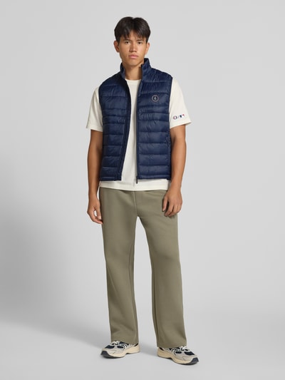 Mannelijk model draagt donkerblauwe bodywarmer met ritssluiting en ritszakken Model 'KINGSLEY' van JACK & JONES, regular fit, opstaande kraag, ruglengte maat M 65 cm, schouderbreedte 42 cm, borstwijdte 43 cm, voorkant volledige lichaamsopname.