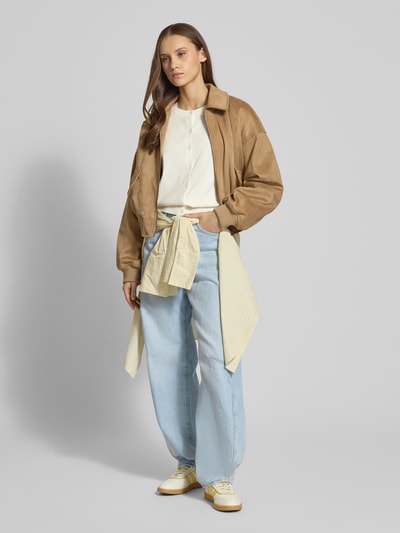 Modelka nosi Strick-Cardigan aus Viskose-Mix mit langen Ärmeln von Review, krój regular fit, długie rękawy, guzikowe zapięcie, haftowane logo, ściągacze na rękawach i u dołu, długość pleców w rozmiarze S: 53 cm, długość rękawa w rozmiarze S: 63 cm, jasne kolory, miękka tekstura, widok całej sylwetki z przodu.