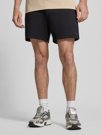 Męski model trägt Regular Fit Shorts aus Baumwoll-Mix von Tommy Jeans, efekt: jednolity kolor, dzianina dresowa, detal z logo, tunel, elastyczny ściągacz, kieszeń z tyłu, wpuszczane kieszenie, mieszanka bawełny, Ganzkörperansicht von vorne.
