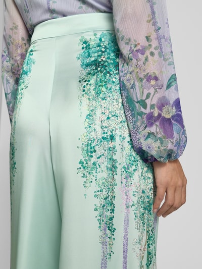 Frauenmodel trägt Hose aus Satin mit weitem Bein von Marc Cain im Allover-Look, zartgrün mit floralen Mustern, seitlicher Reißverschluss, Bundweite 37 cm, Innenbeinlänge 85 cm, Detailaufnahme Rückansicht.