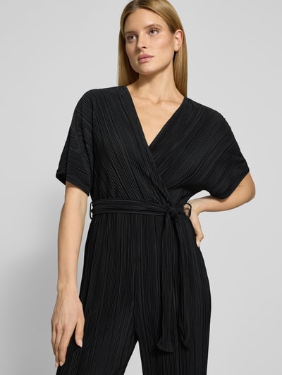 Vrouwenmodel draagt Regular Fit Jumpsuit met V-hals model 'Olinda' van YAS in zwarte plissé-look met stoffen riem, taille accentuerend, korte mouwen, vooraanzicht bovenlichaam.