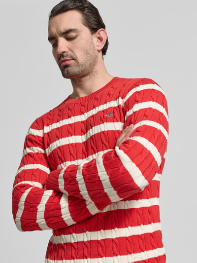 Männermodel trägt Slim Fit Pullover in Strick-Optik von Gant in Rot mit weißen Streifen, reiner Baumwolle, Nahaufnahme Oberkörper.