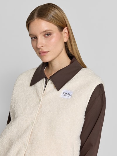 Frauenmodel trägt Regular Fit Weste in Teddy-Optik Modell 'AMALIA' von VILLA SOPHIE, cremefarbenes Teddyfell, Label-Patch, Nahaufnahme Oberkörper.
