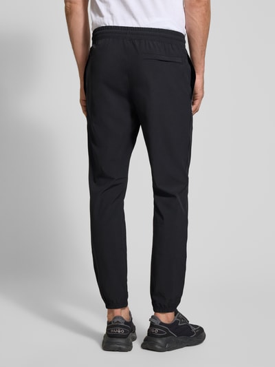 Männermodel trägt Regular Fit Sweatpants mit Logo-Print Modell 'Vibe' von Under Armour, schwarzer Elastischer-Material-Mix, Gesäßtasche, Elastikbund, Ganzkörperansicht Rückansicht.