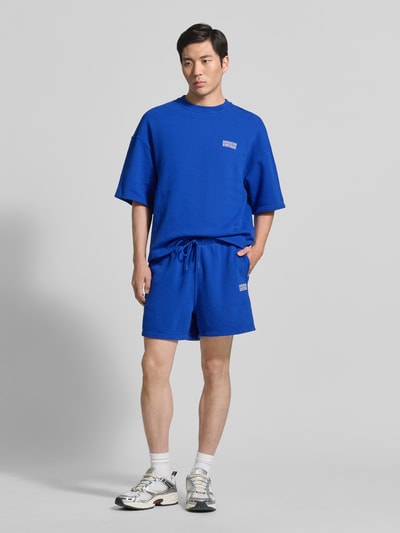 Männermodel trägt Herren T-Shirt mit Logo Modell 'PLIZZY' von American Vintage in Blau, Reine Baumwolle, Relaxed-Fit, Rundhalsausschnitt, Ganzkörperansicht von vorne.