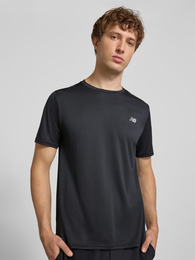 Męski model nosi Funktionsshirt mit Rundhalsausschnitt und Logo od New Balance, czarny, logo, krój regular fit, okrągły dekolt, długość tyłu 69 cm w rozmiarze M, widok całej sylwetki z przodu.